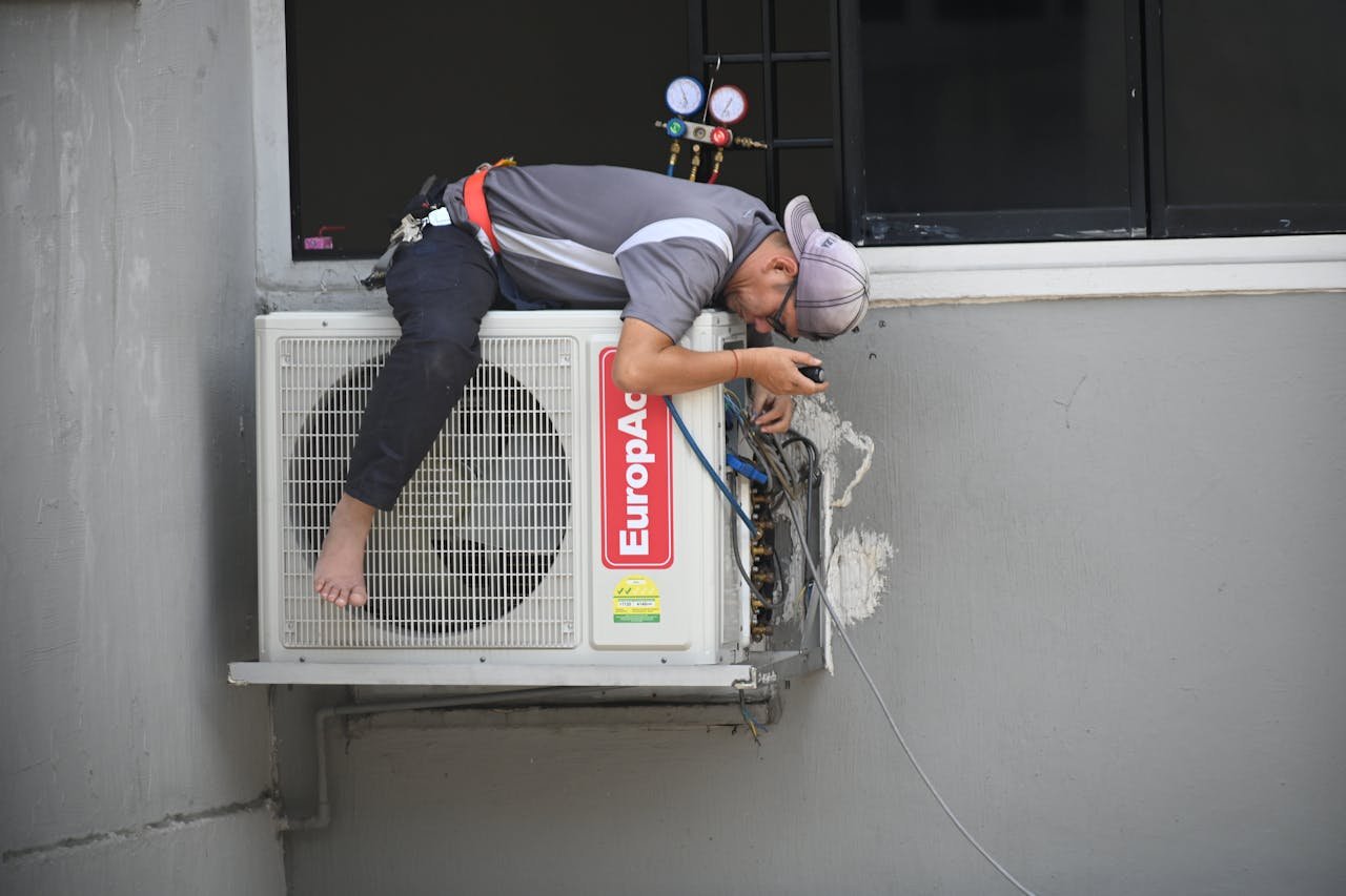 cta-02 A technician skillfully repairing an outdoor air conditioning unit mounted on a building wall.